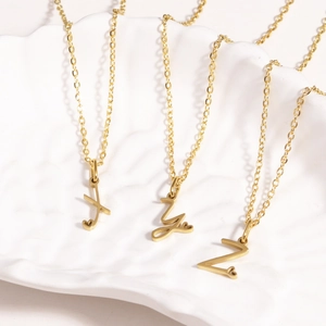 Detailed view of three gold alphabet heart necklaces X Y Z on a white shell tray