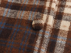 Macro detail of brown plaid tweed dress featuring fabric-covered round buttons