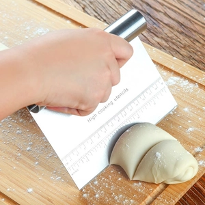 Stainless steel dough scraper with dual scale measurements used on wooden board
