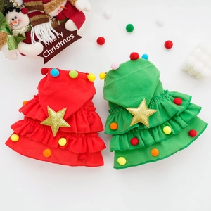 Flat lay of red and green Christmas pet outfits with stars and pom-poms on festive background