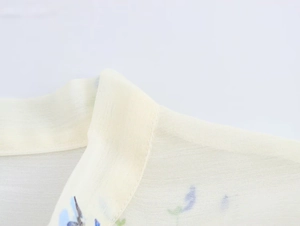 Dettaglio della camicetta in chiffon giallo chiaro con stampe floreali e collo a fiocco