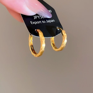Macro shot of gold-plated ripple hoop earrings featuring textured irregular wave design