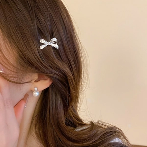 Close-up of silver metal bow hair clip and pearl rhinestone earrings on a model