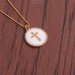 Detail of a gold plated necklace with a white circular zircon cross pendant on wood