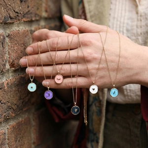 Detailed view of six colorful enamel charms on gold necklaces held by a hand