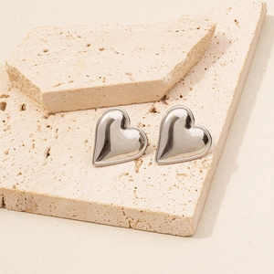 Detailed view of silver heart stud earrings on beige stone with a polished mirror finish