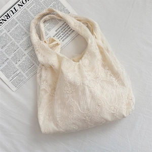 Detailed close-up of lace embroidery on a soft cream white tote bag over a newsprint base