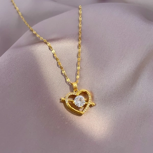 Close-up of golden heart arrow pendant with crystal inlay on grey silk fabric