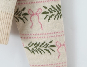 Detail of knit sweater sleeve featuring pink bow jacquard and green pine branch patterns