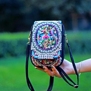 Detail of vibrant floral bird embroidery on black fabric crossbody bag held in hand
