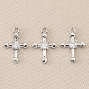 Detail of three silver baroque cross pendants with heart designs and clear gemstones