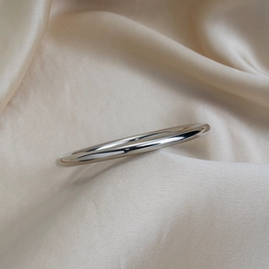 Polished silver stainless steel bangle displayed on champagne silk fabric background