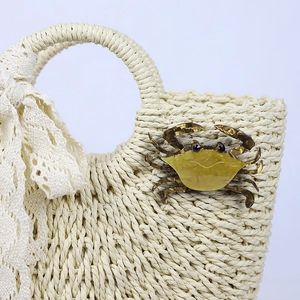 Handmade acrylic crab brooch with yellow resin shell pinned on a beige woven straw bag