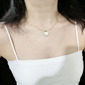 Dettaglio della collana dorata con ciondolo quadrato e cuore bianco indossata