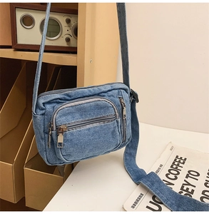 Close-up of blue denim crossbody bag featuring multi-layer zippers and adjustable strap