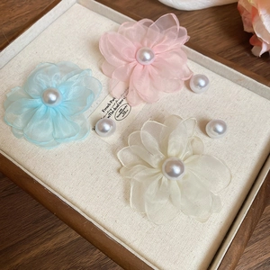 Detailed view of light blue, pink, and white chiffon flower earrings with pearls on a box