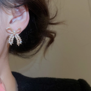 Close-up of elegant gold bow earrings with sparkling cubic zirconia on a model's ear