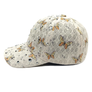 Detailaufnahme einer cremefarbenen Spitzenkappe mit Schmetterlingsmuster und Strass