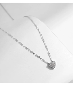 Macro shot of silver heart pendant with shimmering pavé diamonds on a thin chain