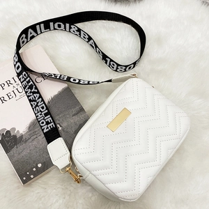 White quilted crossbody square bag with black embroidered wide strap on white plush surface
