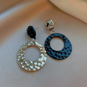 Detail of asymmetric silver and black hammered hoop earrings on beige silk fabric