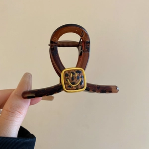 Detail of leopard print hair claw clip with smiley face motif held in hand