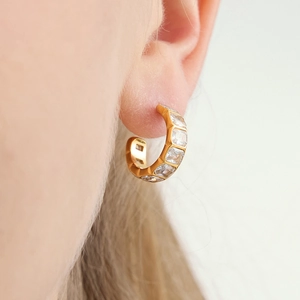 Close-up of gold C-shaped titanium earrings with square zircon inlay on ear