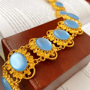 Detailed close-up of a vintage gold bracelet featuring oval blue stones and floral design