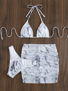 Flat lay of marble print three-piece bikini set with ruched mini skirt on wood surface