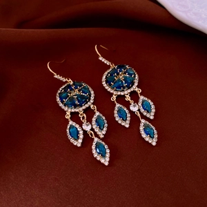 Detail of French court style gold dreamcatcher earrings with blue zircons on silk fabric