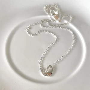 Minimalist 925 sterling silver heart necklace with orb engraving on white ceramic plate