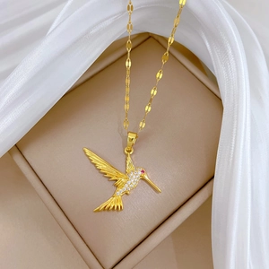 Macro shot of gold hummingbird necklace with clear and red crystals on beige silk