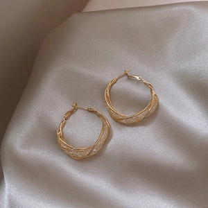 Detail of twisted gold hoop earrings with zircon pavé on champagne silk fabric