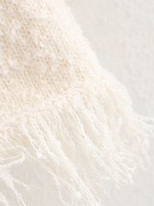 Detail shot of cream knit fabric texture with decorative fringe and soft boucle yarn finish