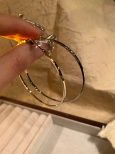 Macro detail of large silver circular hoop earring held against a neutral background