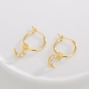 Golden hollow moon earrings with zircons on white ceramic tray, professional fashion jewelry