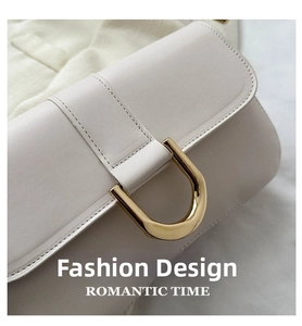 Detailed macro view of the large gold U-shaped metal buckle on a beige leather handbag