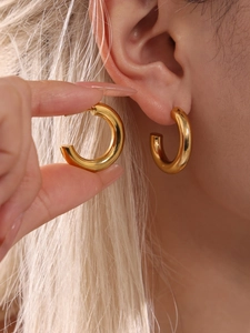Macro detail of gold-plated chunky C-shaped hoop earrings with polished finish on model