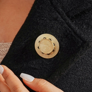 Detailed macro view of a gold woven straw hat brooch on a black wool coat fabric