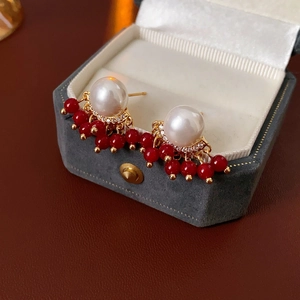 Detail of gold-plated tassel earrings with white pearls and red beads in a jewelry box
