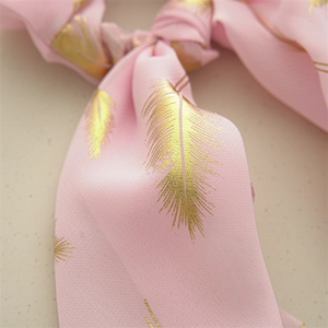 Detailed view of pink chiffon scrunchie with golden feather prints and soft texture