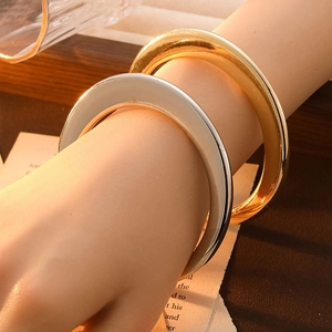 Close-up of stacked gold and silver minimalist open bangles on a stylish wooden base
