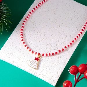 Detail of red and white beaded Christmas necklace with golden tree pendant on green background