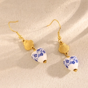 Detail of heart-shaped blue and white ceramic earrings with 18K gold plated shell hooks