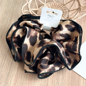 Close-up of leopard print satin scrunchie with a smooth texture and rich folds on wood