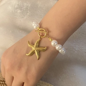 Detail of a white pearl bracelet featuring a golden starfish pendant and T-bar toggle clasp