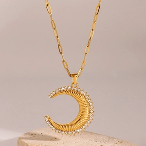 Détail d'un pendentif lune doré avec texture rayée et pierres de zircone blanches
