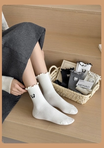 Detail of white cotton crew socks with bow embroidery and ruffled edges on wooden stairs