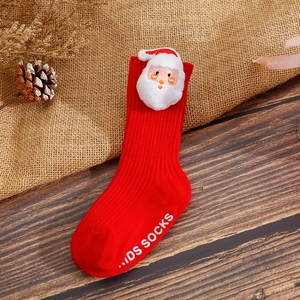 Detail of red Christmas baby sock with Santa Claus 3D decor and anti-slip sole on wood