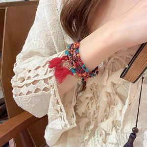 Detail of bohemian multilayer beaded bracelet with red tassels on a model wearing lace